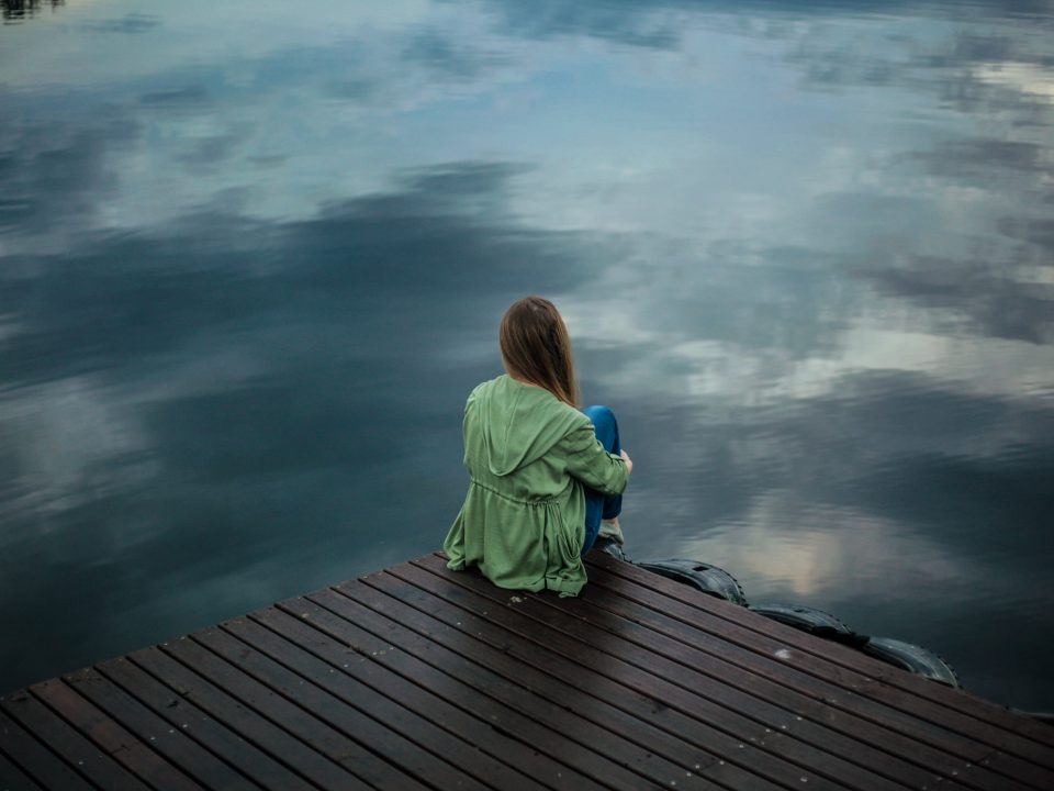 woman sitting on dock near body of water