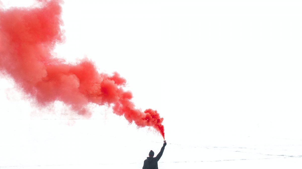 selective color photography of person holding orange gas smoke standing on snow