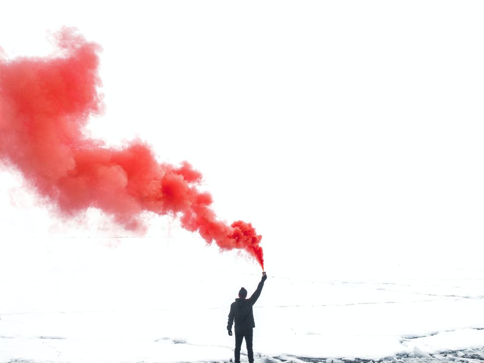 selective color photography of person holding orange gas smoke standing on snow