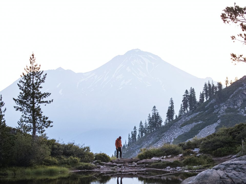 person standing on rock near lake and mountain during daytime