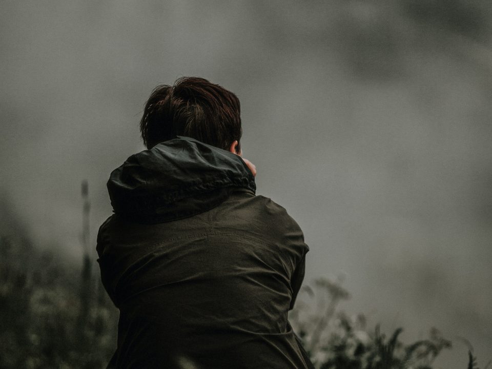 selective focus photo of person in black hooded jacket sitting on green grass field at daytime