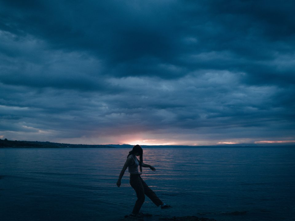 woman in black dress standing on seashore under cloudy sky during daytime