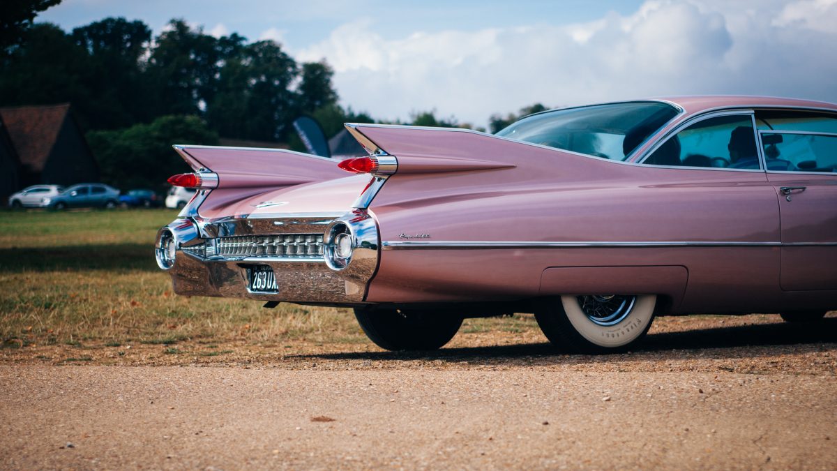vintage pink muscle car parked near field of grass