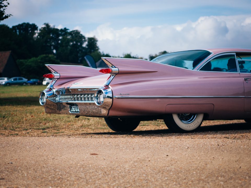 vintage pink muscle car parked near field of grass