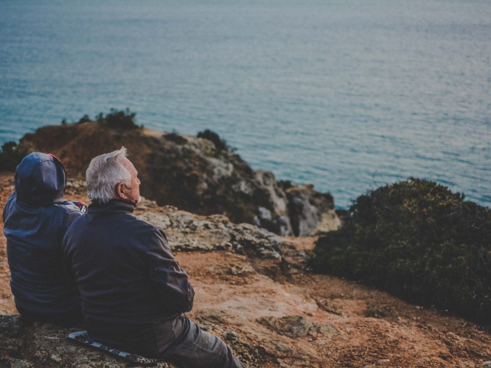 two person sitting on rock staring at body of water during daytime