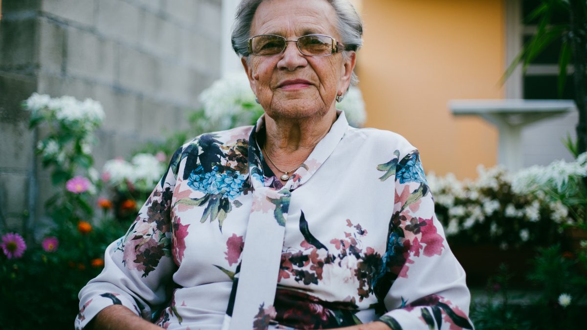 woman wearing white and multicolored floral top front of flower garden