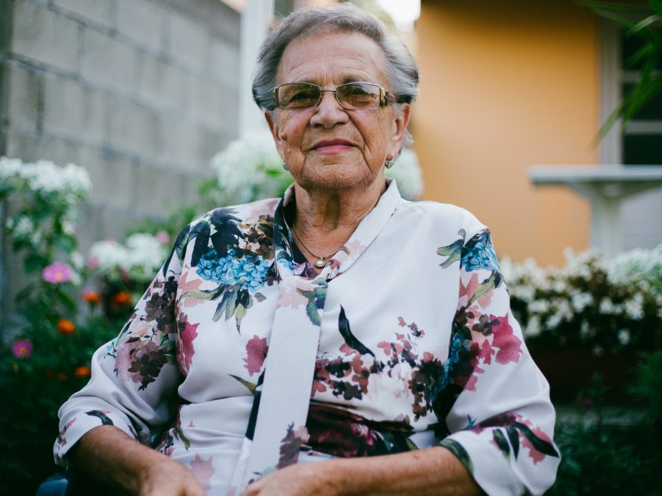 woman wearing white and multicolored floral top front of flower garden