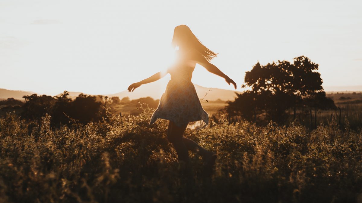 silhouette of woman dancing in the middle of grass field