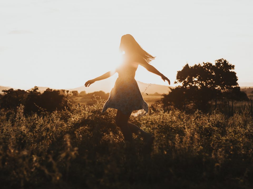 silhouette of woman dancing in the middle of grass field