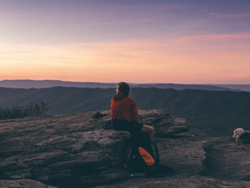 person sitting on boulder overlooking mountain during golden hour