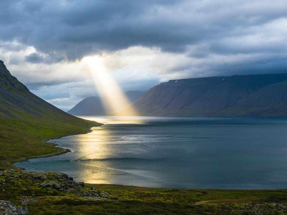 sun reflection on calm water near green mountains