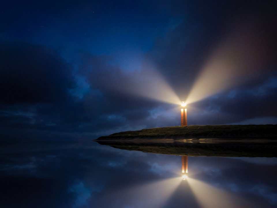 lighted brown lighthouse beside body of water