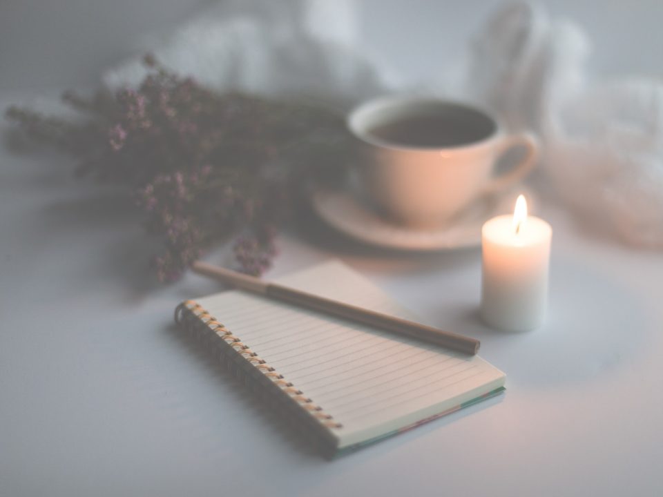 white candle on white ruled paper beside white ceramic mug