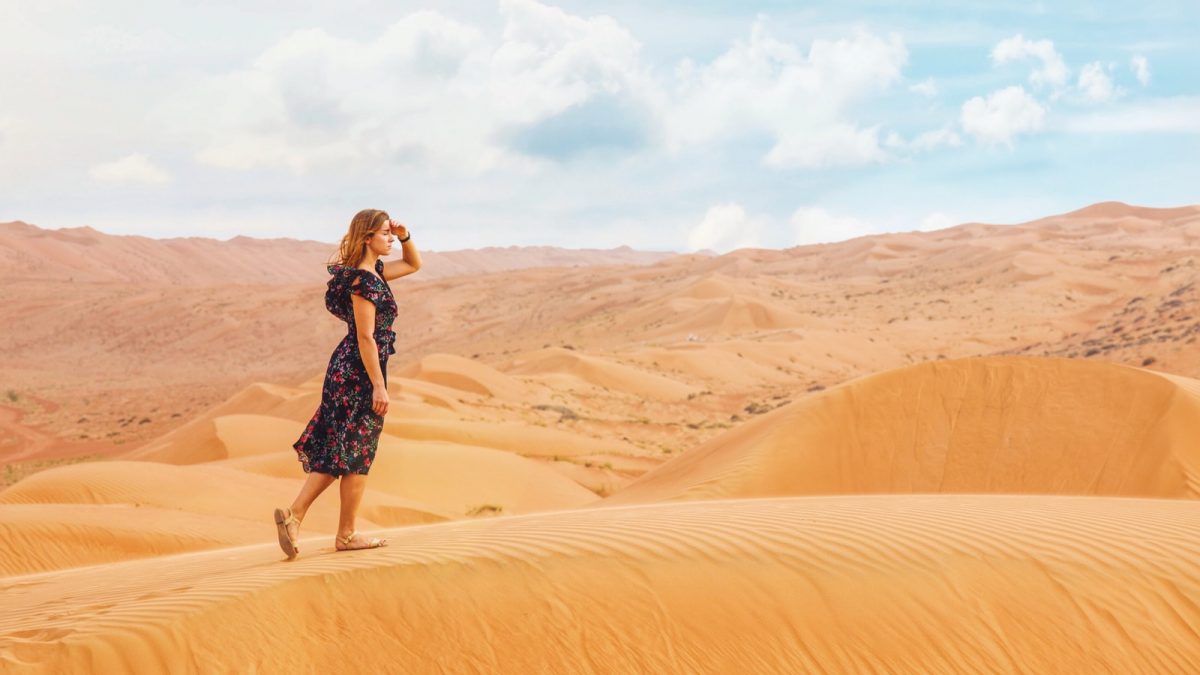 woman walking on sand dunes during daytime