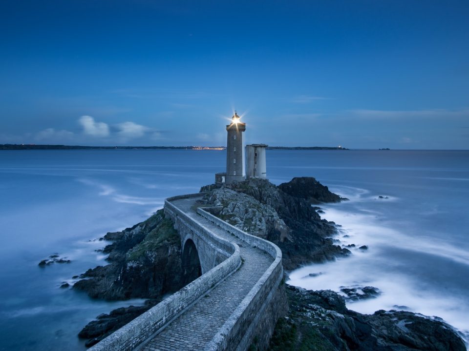 gray lighthouse on islet with concrete pathway at daytime