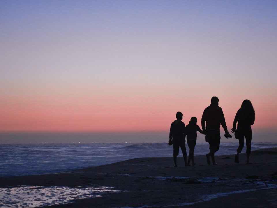 silhouette of 3 men and woman standing on beach during sunset