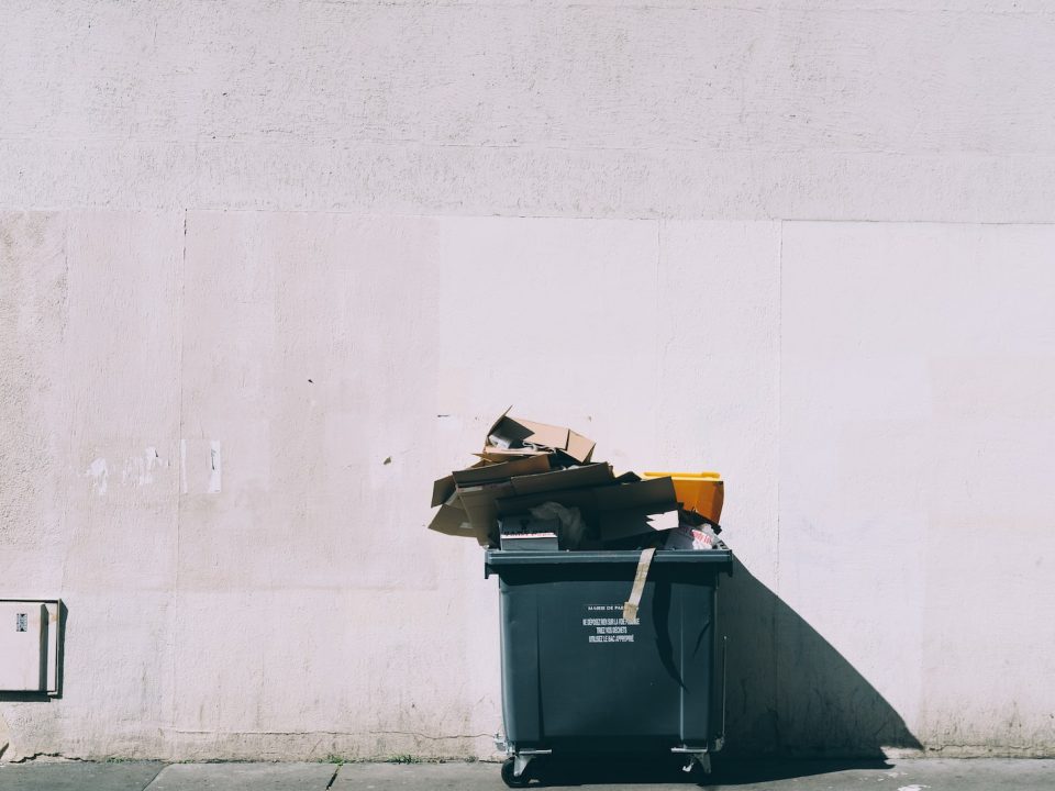 black plastic garbage bin with wheels beside wall