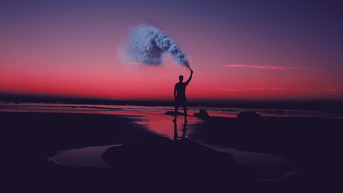 silhouette of man standing on seashore holding smoke can