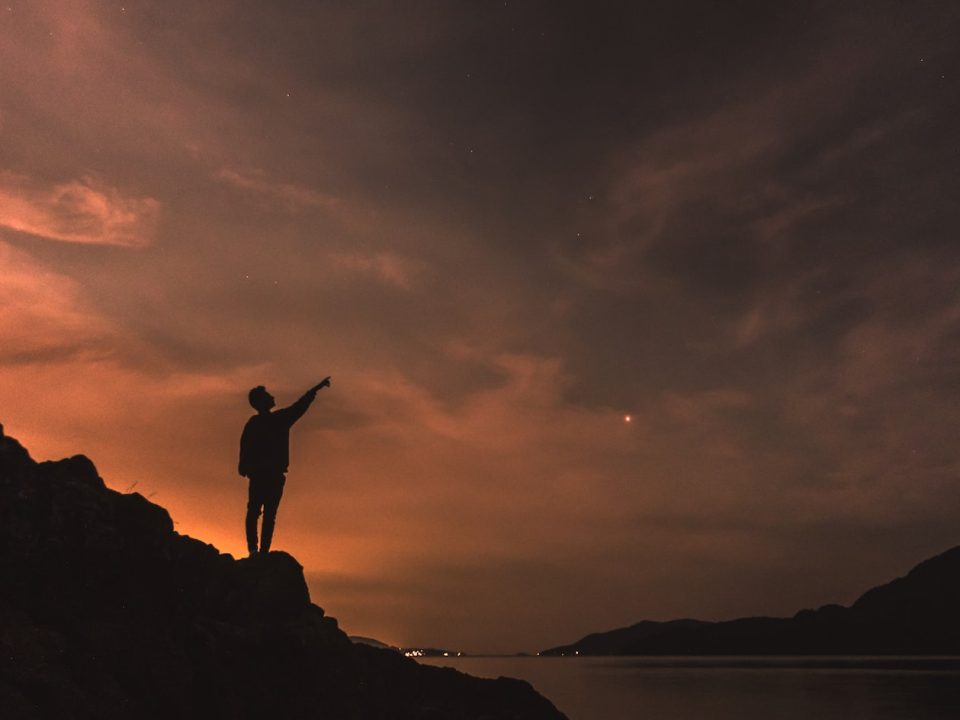 silhouette photography of person standing on rock beside body of water