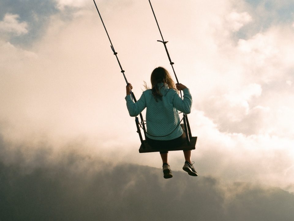 girl in blue hoodie sitting on swing under cloudy sky during daytime