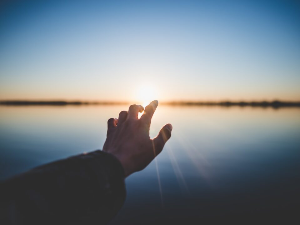 landscape photography of person's hand in front of sun