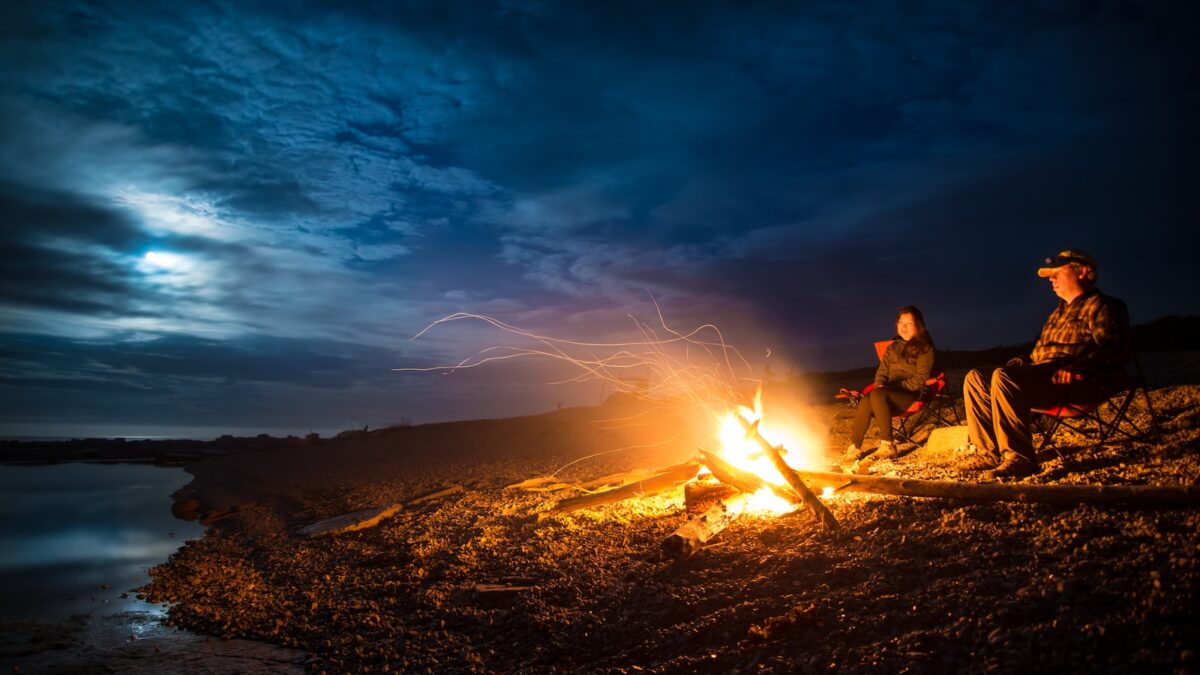 man and woman standing near bonfire on seashore during night