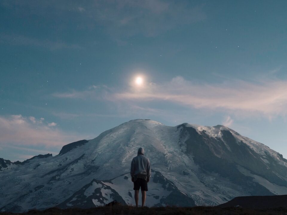 man standing on grass field overlooking mountain