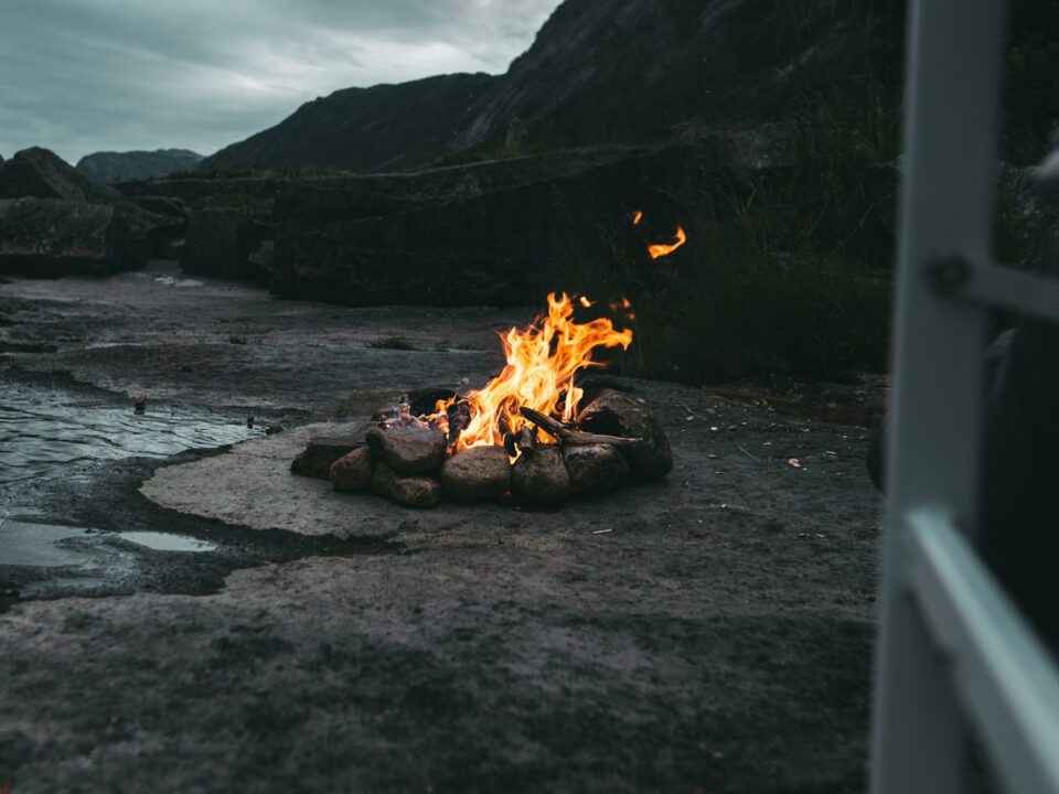 fire on black sand near body of water during daytime