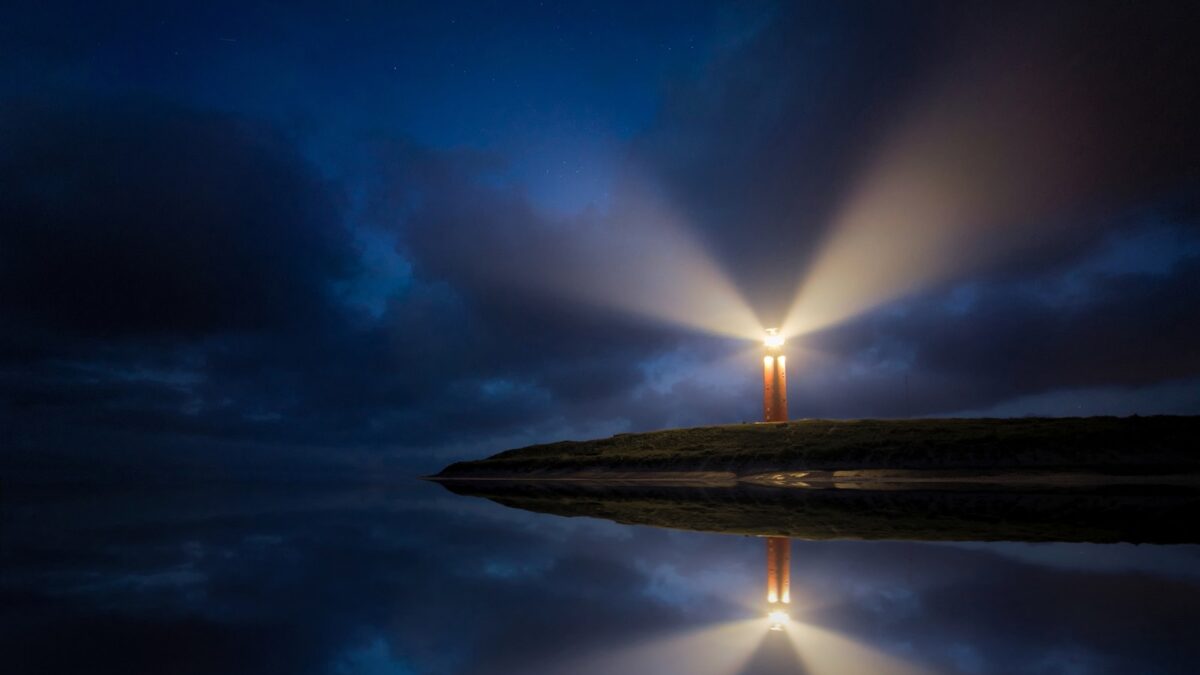 lighted brown lighthouse beside body of water