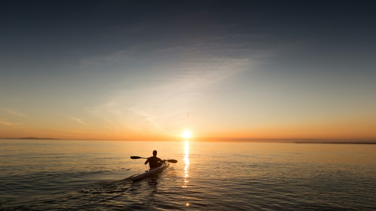 man riding kayak on water taken at sunset