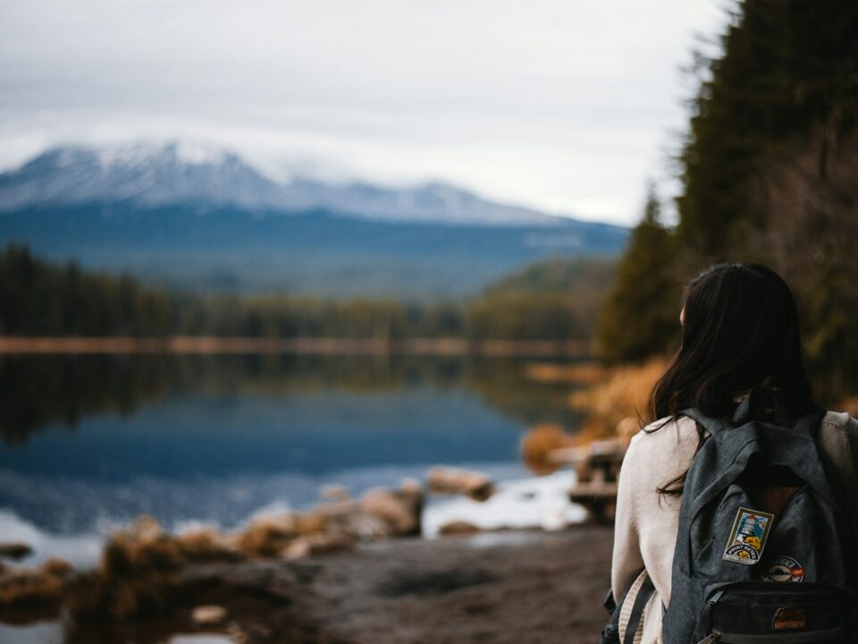 woman in gray jacket standing near lake during daytime
