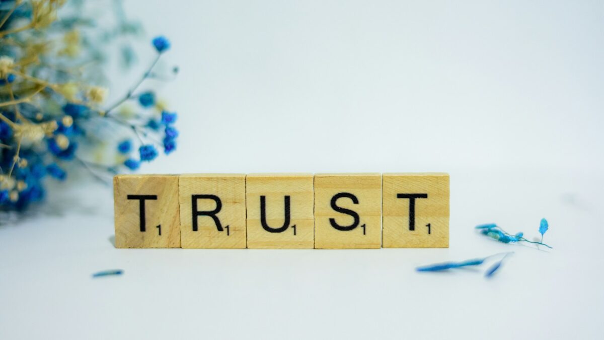 a wooden block that says trust, surrounded by blue flowers