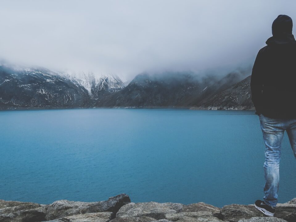 man standing on cliff facing bod of water