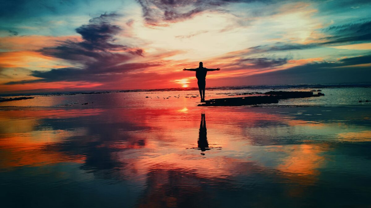 silhouette of person standing on rock surrounded by body of water