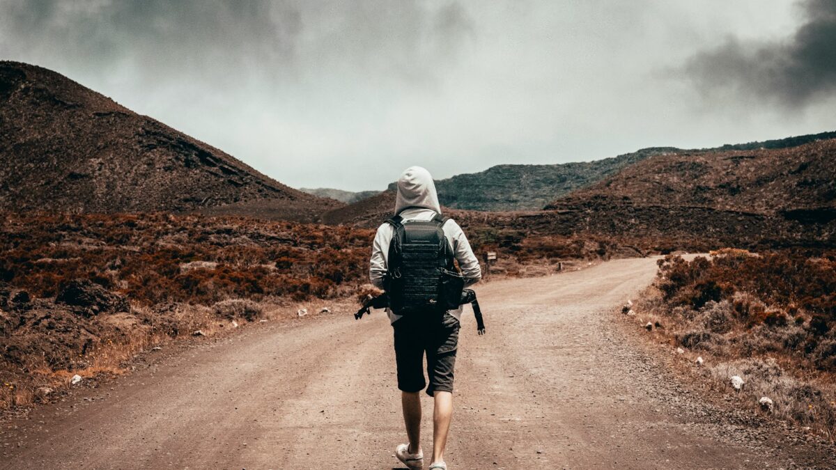 man in gray hoodie carrying backpack walking under the sun