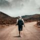 man in gray hoodie carrying backpack walking under the sun