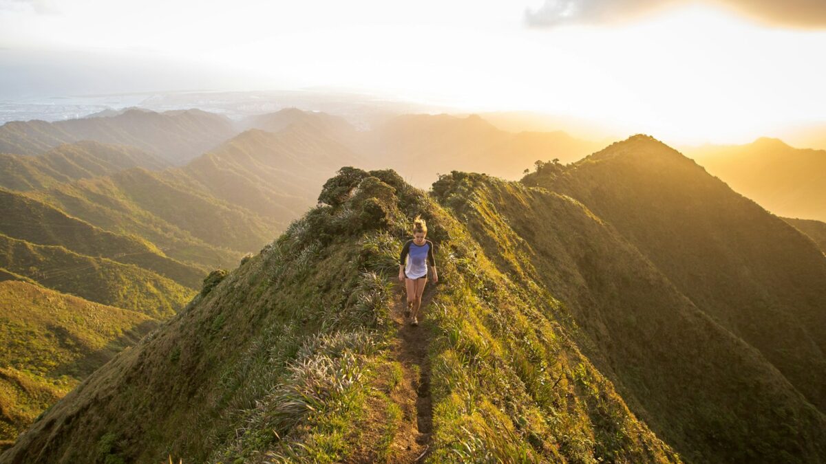 woman walking on pathway on top of hill at golden hour