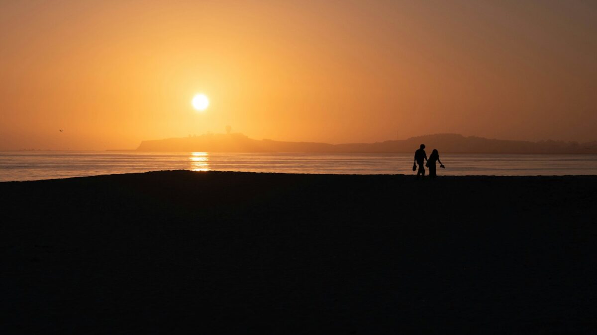 Two people walking on a beach at sunset