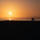 Two people walking on a beach at sunset