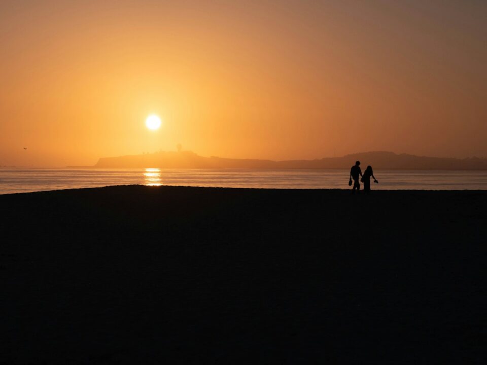 Two people walking on a beach at sunset