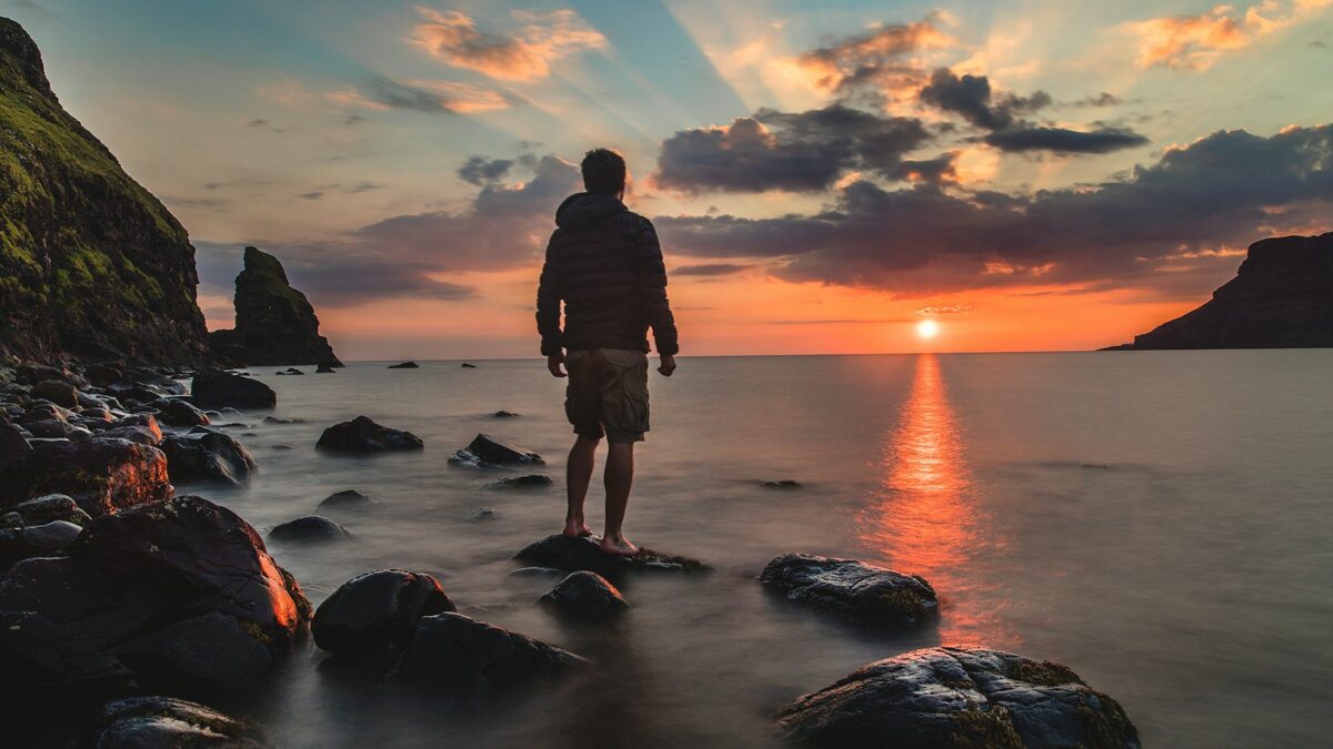 man standing on stone looking at sunset