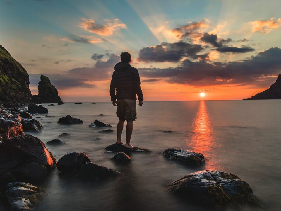 man standing on stone looking at sunset