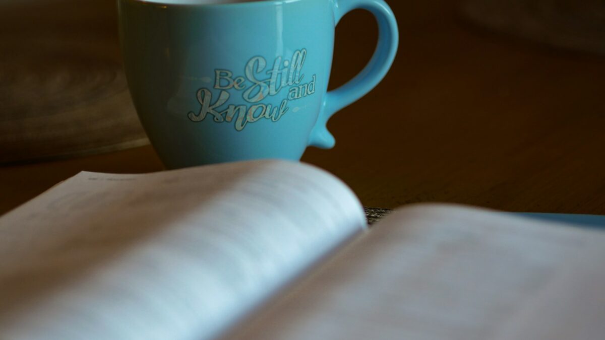 shallow focus photography of open book beside blue ceramic cup