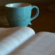 shallow focus photography of open book beside blue ceramic cup