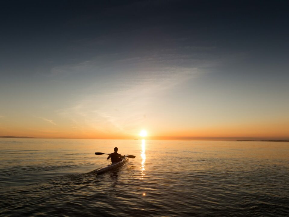 man riding kayak on water taken at sunset