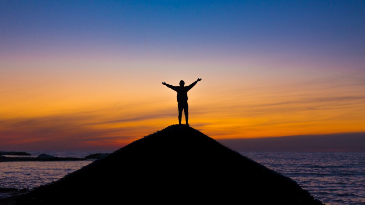 silhouette of person standing on rock during sunset