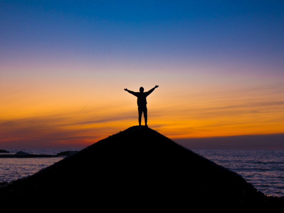 silhouette of person standing on rock during sunset