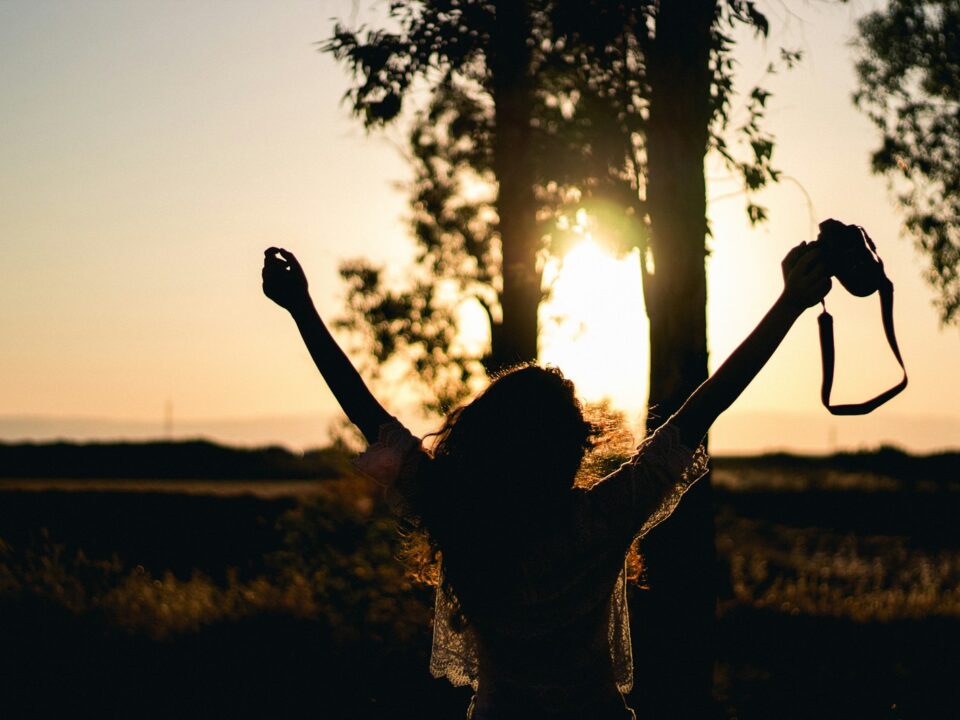 silhouette photo of woman raising her hands while holding DSLR camera