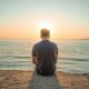 man sitting on sand front of sea during golden hour