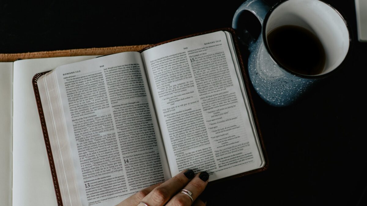 person reading book beside white ceramic mug with coffee